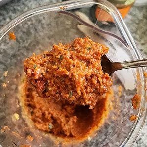 Spoon of sun-dried tomato pesto with a glass jar beneath.