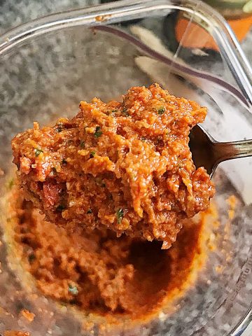 Spoon of sun-dried tomato pesto with a glass jar beneath.