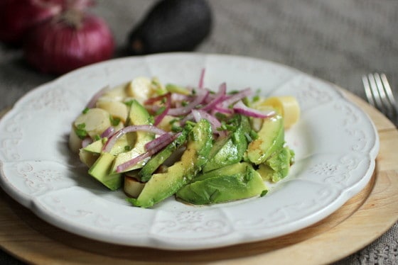 White plate with avocado, hearts of palm and red onion, whole vegs in background