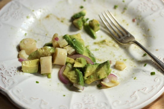 Remains of avocado and heart of palm salad on white plate, a silver fork