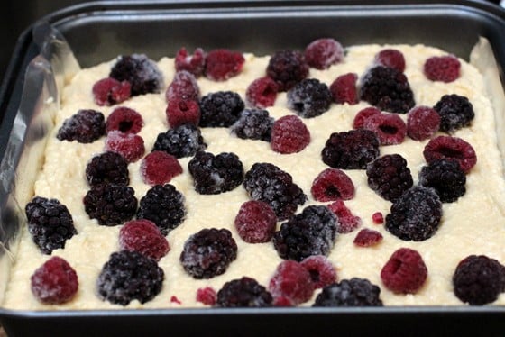 Unbaked cake batter topped with berries on a metal square pan