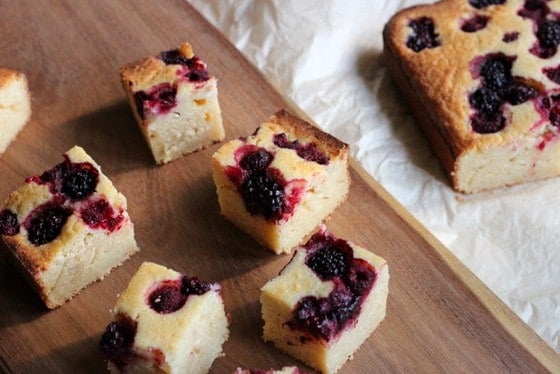 Berry Ricotta Squares squares on wooden board, rest of cake on white paper