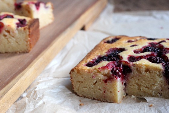 Cut berry ricotta cake on white paper, squares in wooden board beside it