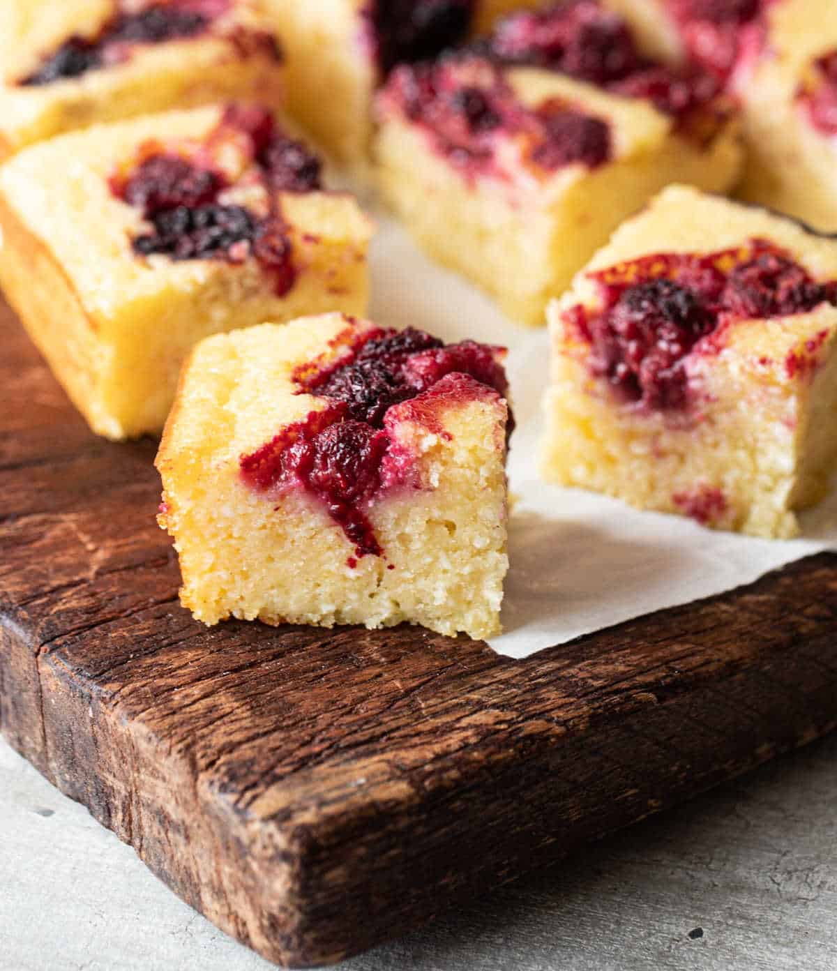 Wooden board with squares of berry ricotta cake.