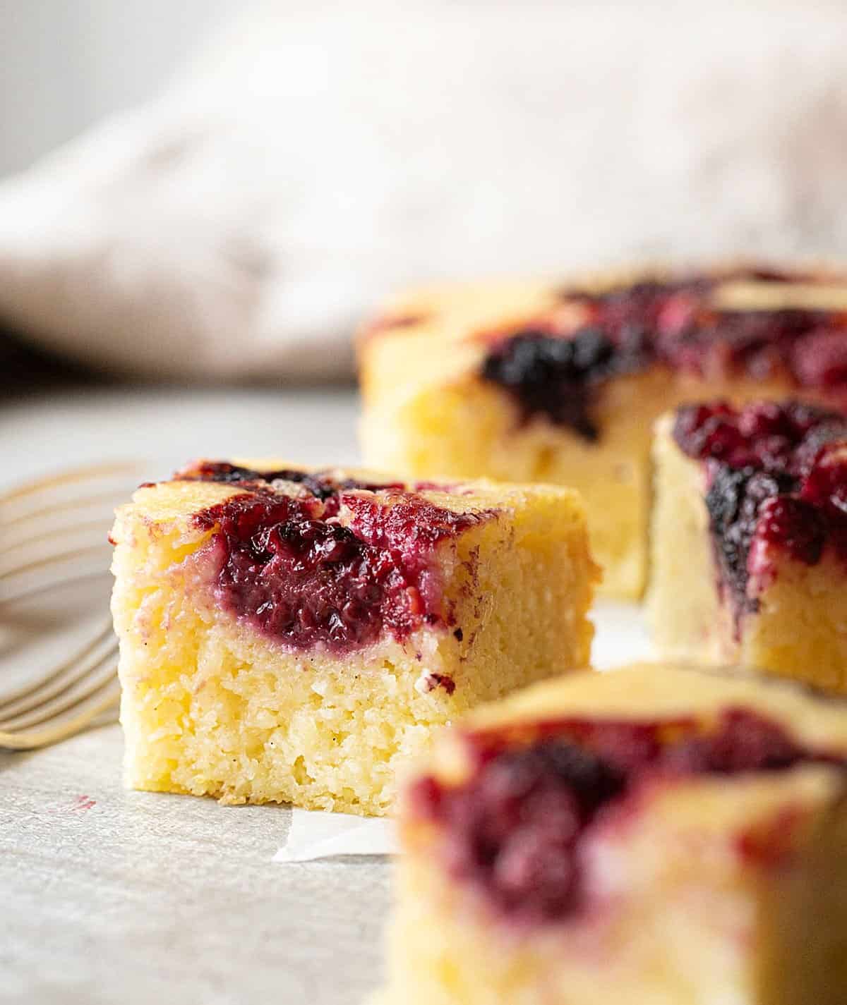 Several squares of ricotta cake with berries on grey surface and background. 