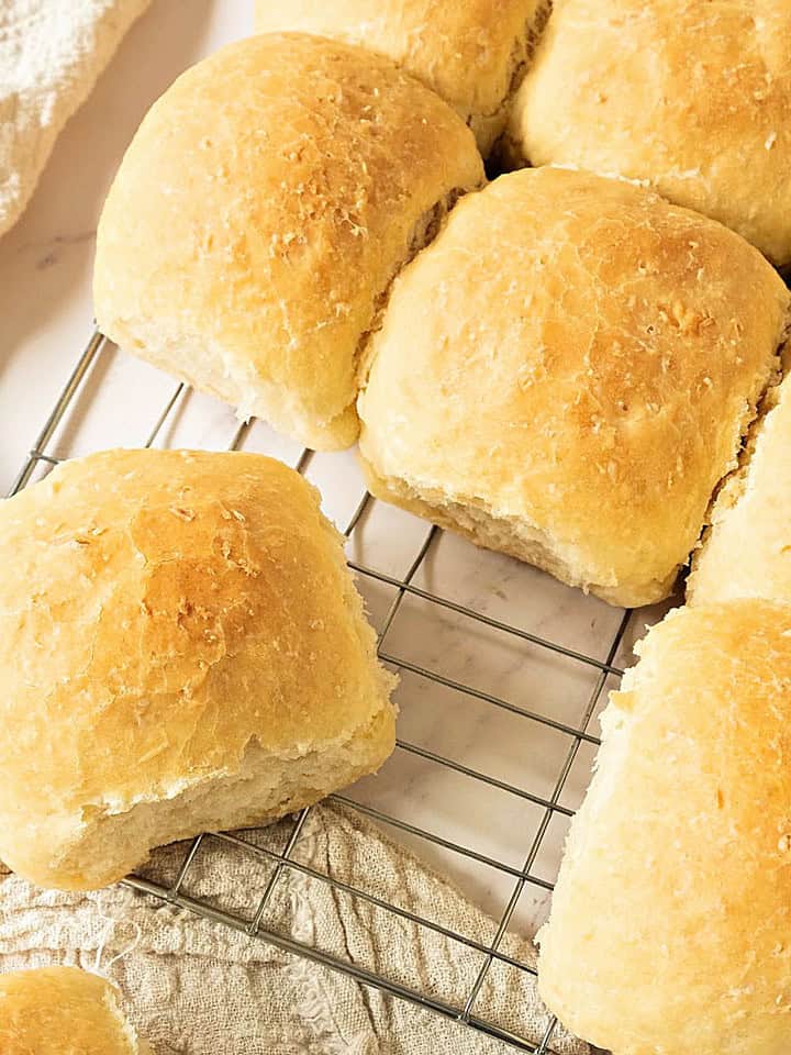 Close-up of wire rack with several coconut buns. Cream-colored cloth.