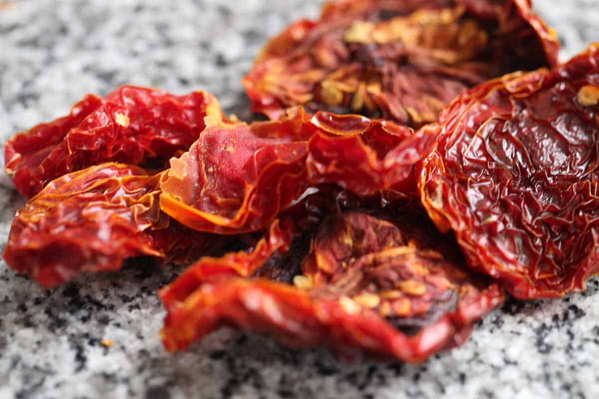 Several sun-dried tomatoes on grey granite surface.