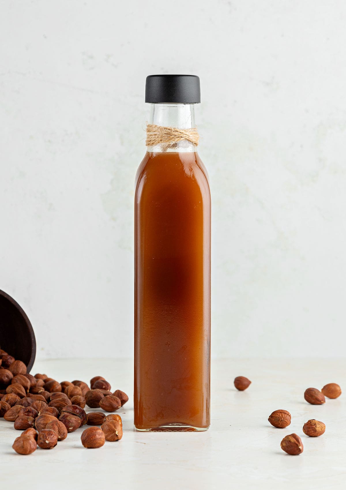 Tall, thin bottle of hazelnut liqueur on a gray beige background. Whole hazelnuts.