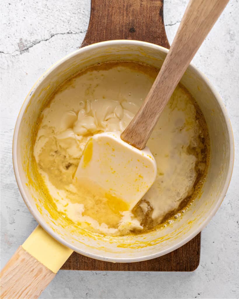 Saucepan with cream and caramel sauce. White spatula. Light gray surface.