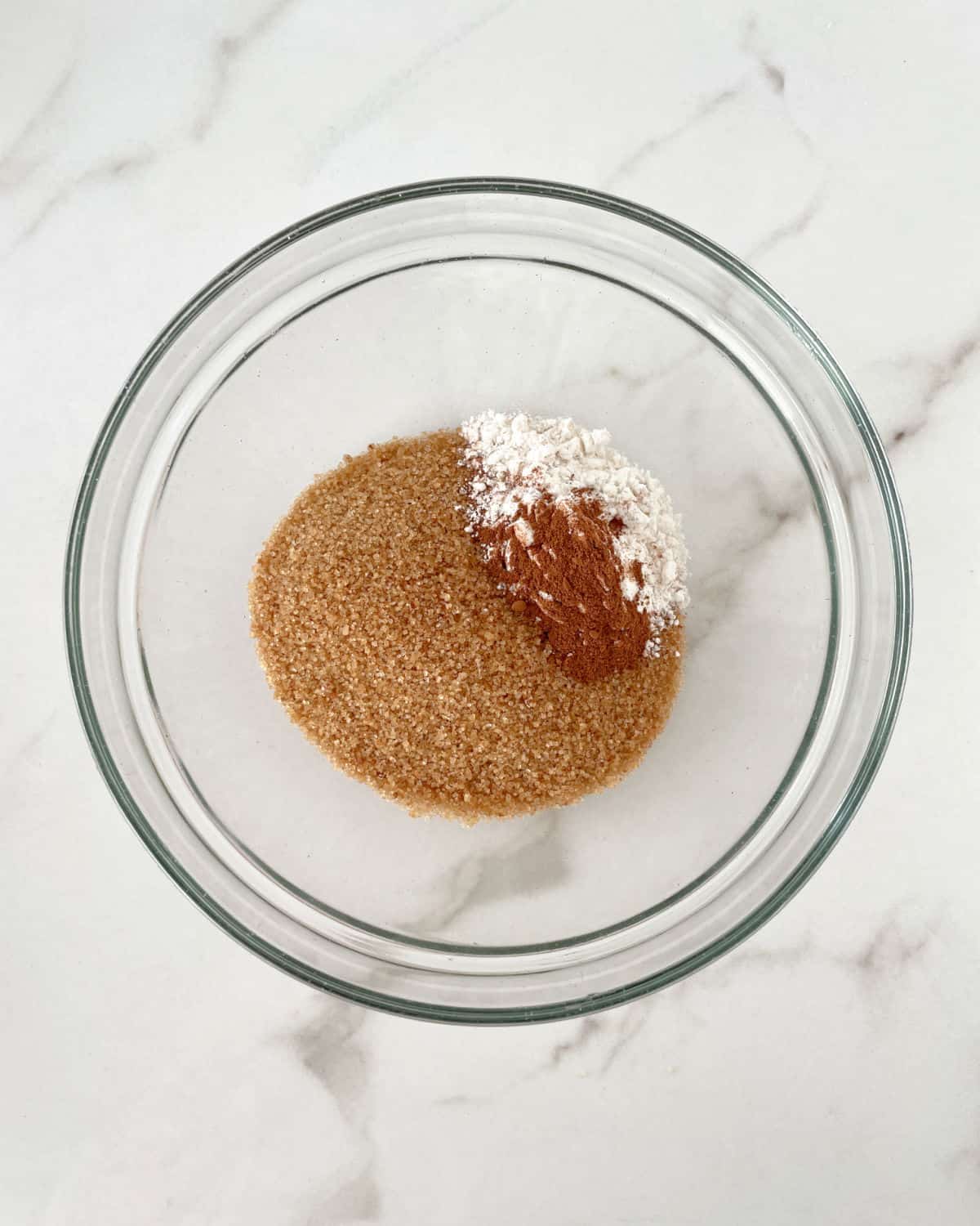 Dry streusel ingredients in a glass bowl on a white marble surface.