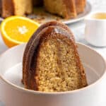 Close up white bowl with caramel glazed bundt cake slice. Orange half, white background.