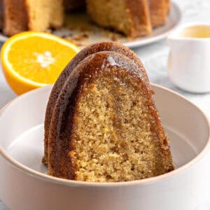 Close up white bowl with caramel glazed bundt cake slice. Orange half, white background.