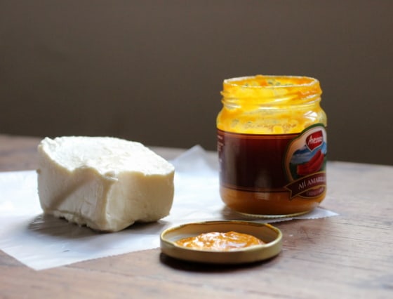 Hunk of queso fresco and jar of yellow pepper paste on wooden table