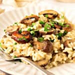 Close up mushroom risotto with chopped parsley on a white plate. Silver fork.