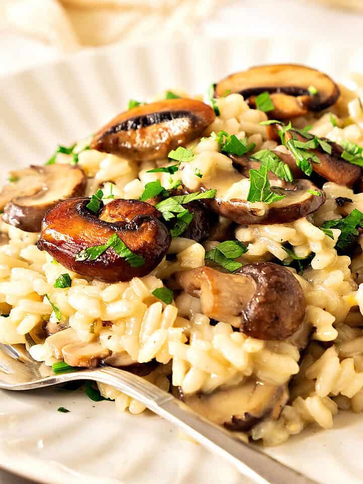 Close up mushroom risotto with chopped parsley on a white plate. Silver fork.