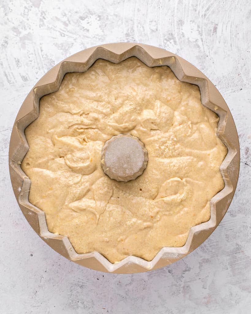 Light gray surface with orange cake batter in a bundt pan.