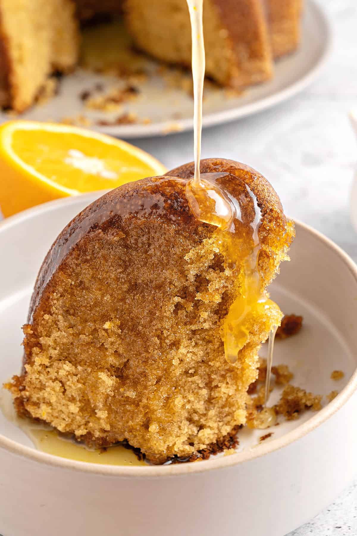 Whitish bowl with slice of bundt cake being glazed with caramel.