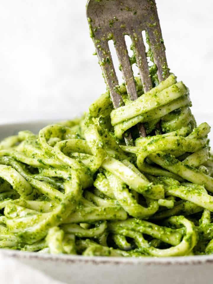 Close up of pesto noodles being forked from a white bowl. Light grey background.