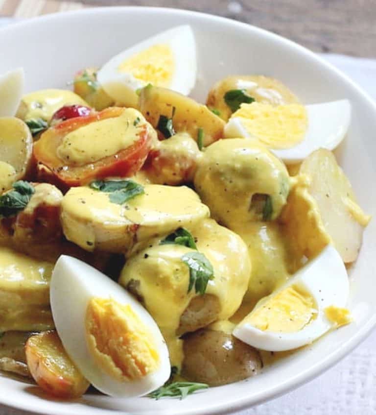 Close up of potato egg salad with yellow pepper sauce in a white bowl.