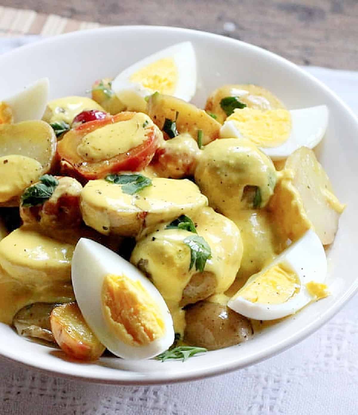 Potato egg salad in a white bowl over white linen placemat.