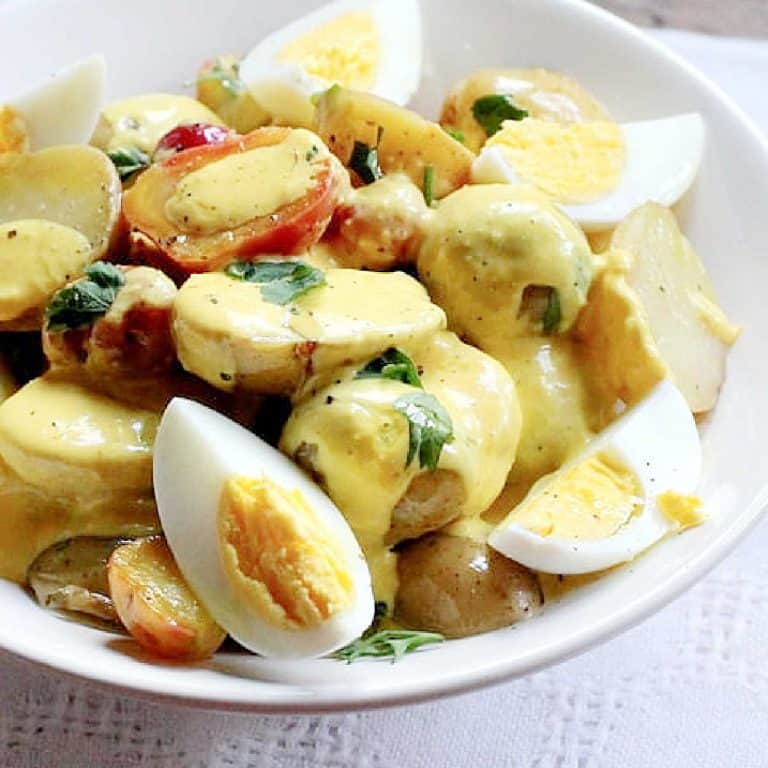 Close up of potato egg salad with yellow pepper sauce in a white bowl.