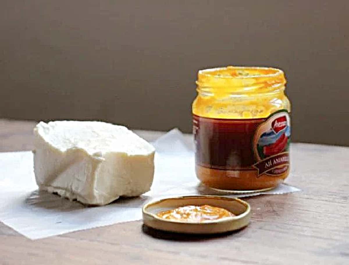 Hunk of queso fresco and jar of yellow pepper paste on wooden table.