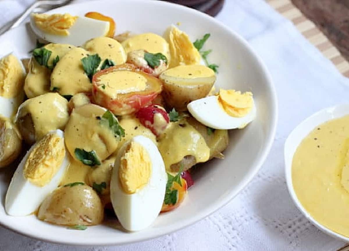 White bowl of Potato Salad, hard boiled eggs, dressing on the side.