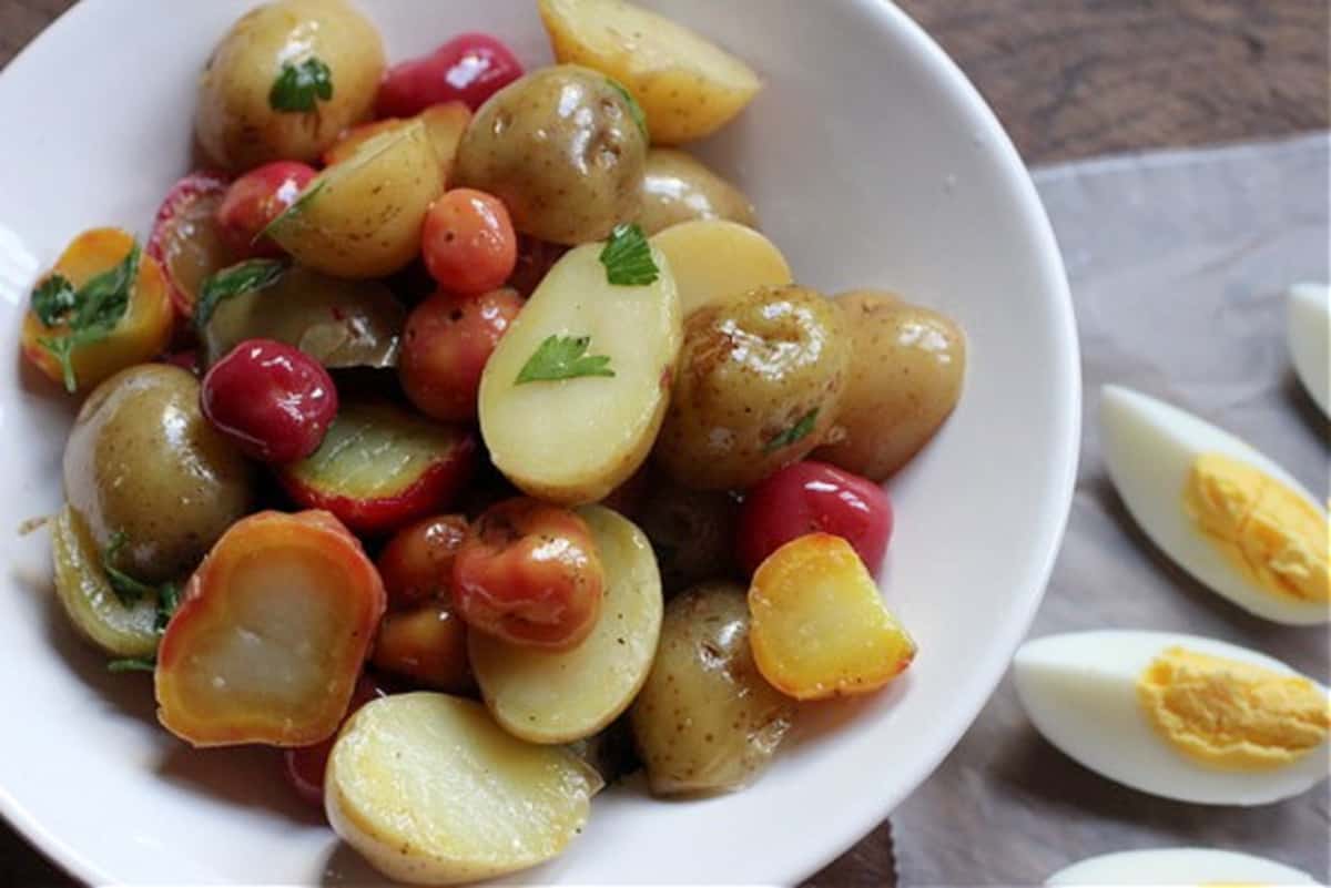 Different small potatoes on white bowl, hard-boiled egg wedges on the table.