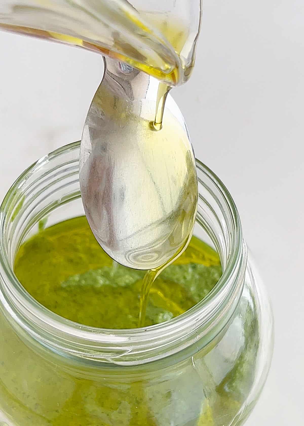 Drizzling oil down the back of a spoon into a jar with pesto.