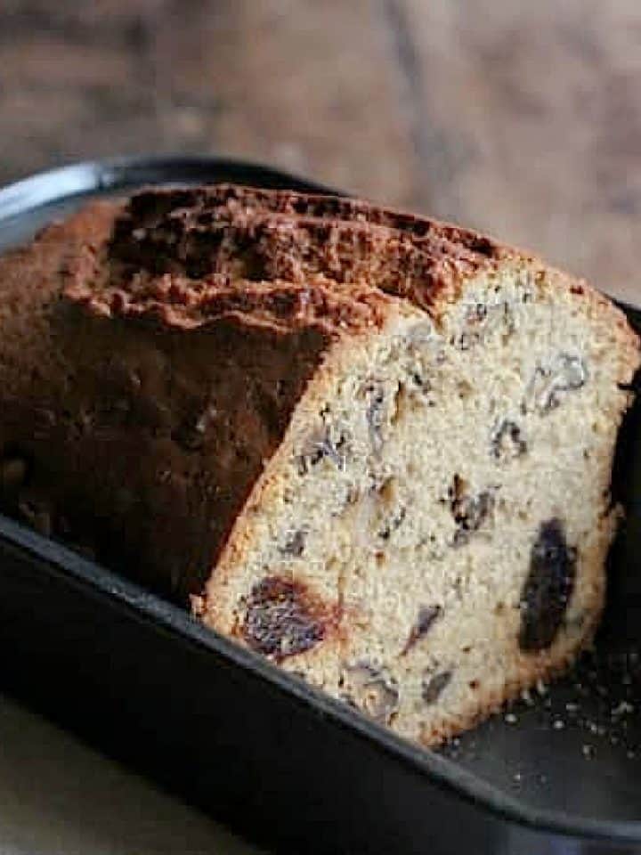 Close up of half load of walnut date bread in a dark metal pan.