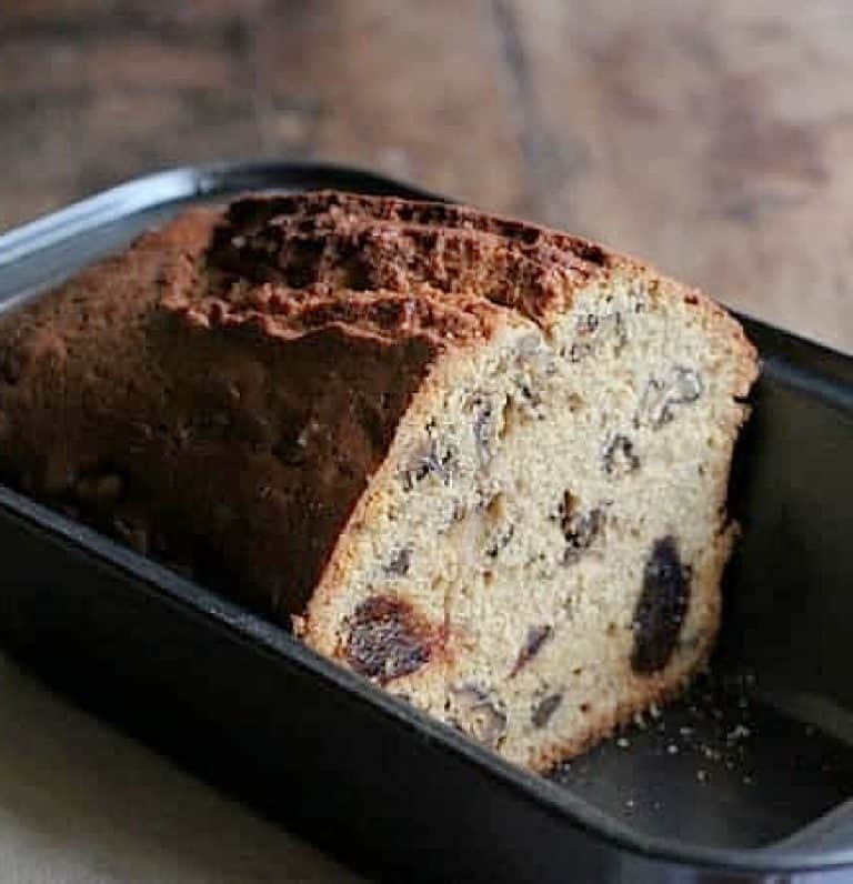 Close up of half load of walnut date bread in a dark metal pan.