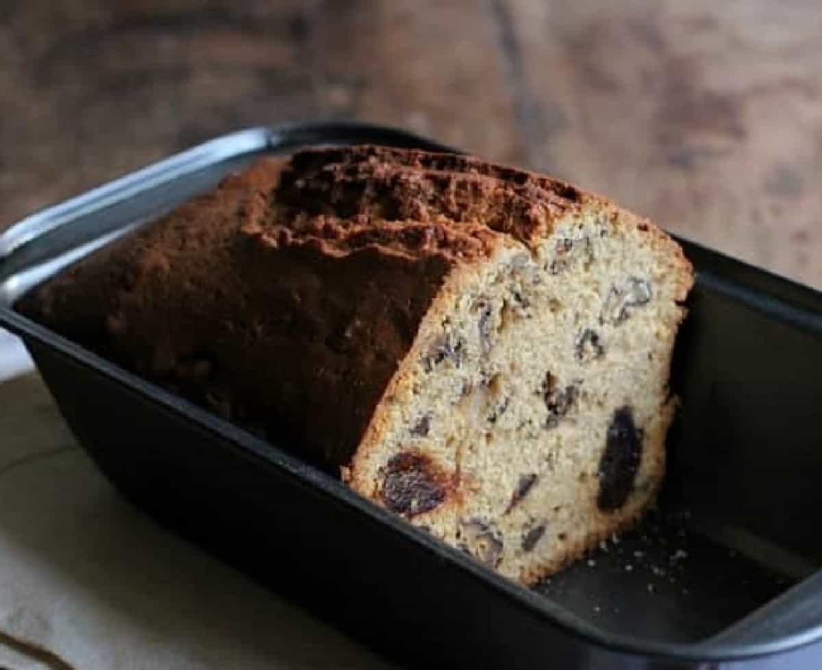 Half date loaf in metal pan on wooden table.