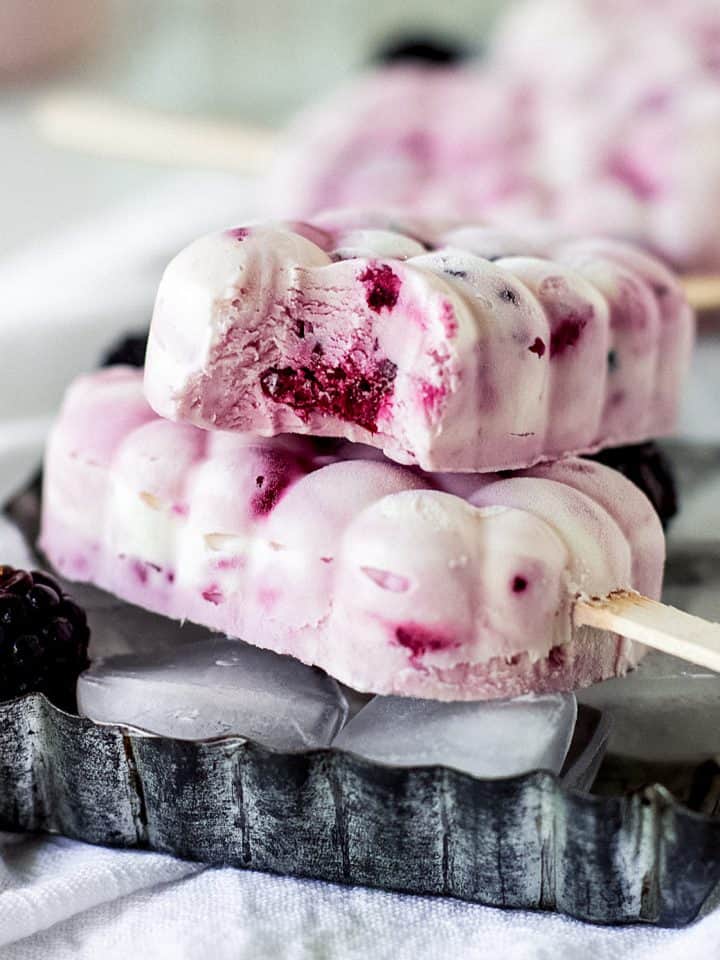 Two white and magenta ice cream paletas on a metal pan, one is bitten