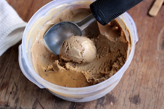 Scooping coffee ice cream from Plastic container on wooden table.