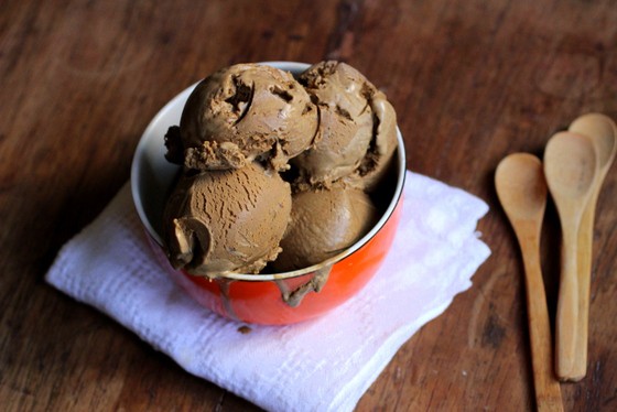 Orange bowl with scoops of coffee ice cream, white napkin, wooden board and spoons.