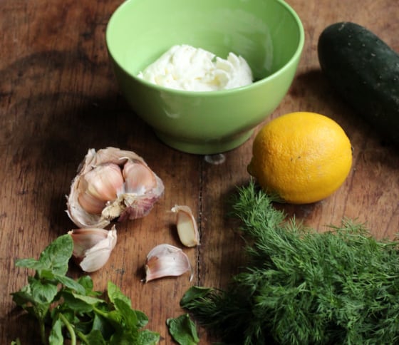 Ingredients on wooden table including garlic, herbs, lemon, bowl with yogurt