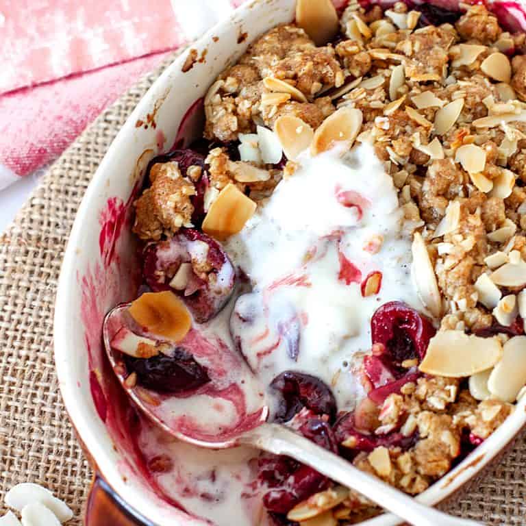 White individual dish with cherry crisp, silver spoon and melted ice cream, rustic background