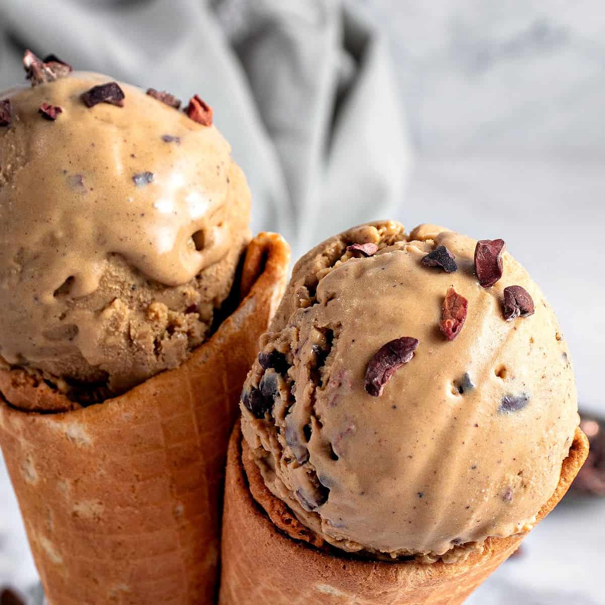 Waffle cones with coffee ice cream and cocoa nibs. Light gray background.