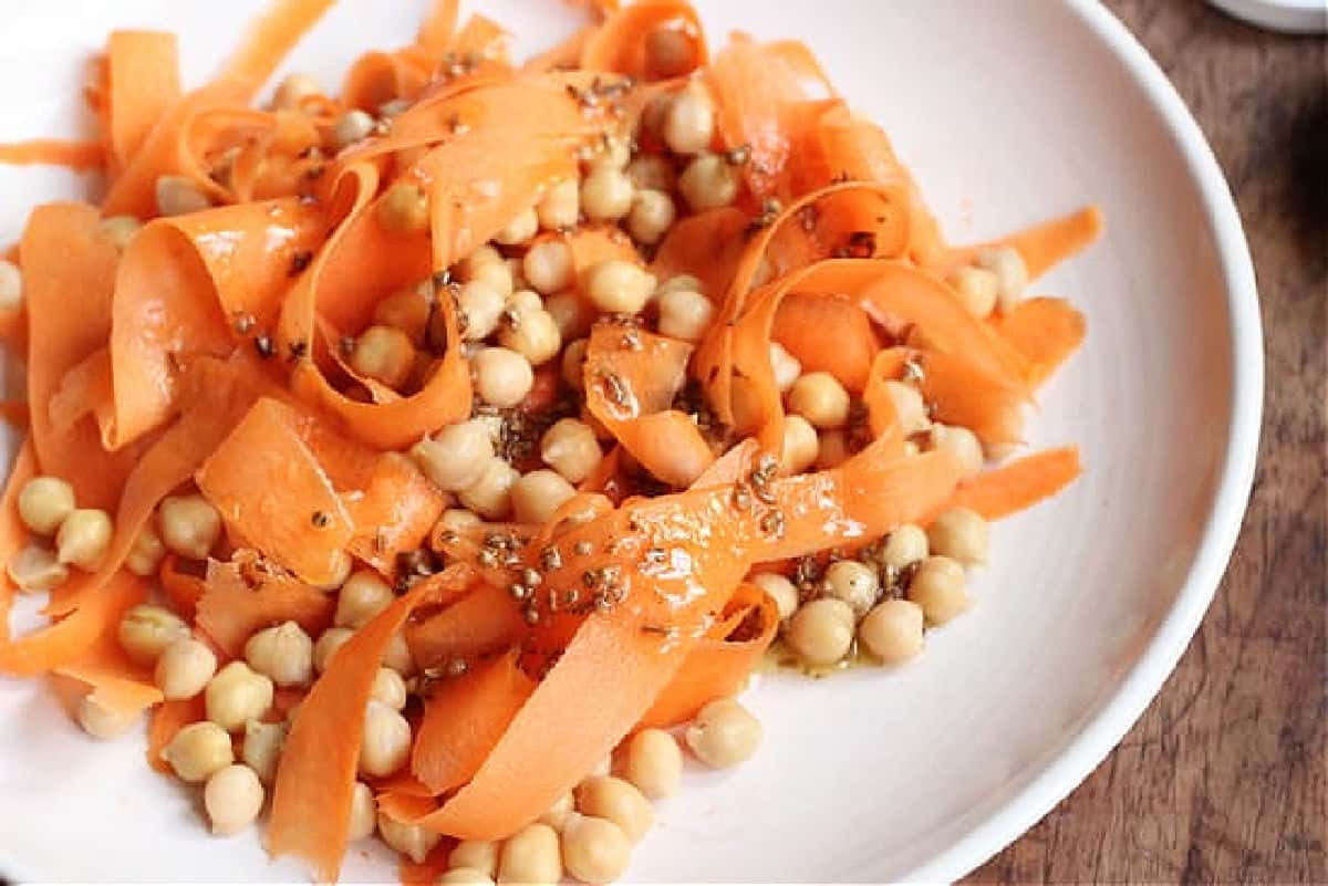 White plate with sliced carrots, chickpeas and dressing.
