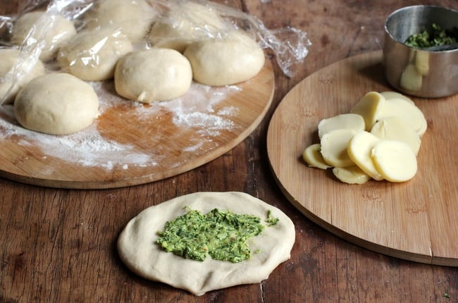 Filling Naan Bread; board with dough balls, slices of cheese, pesto, wooden table