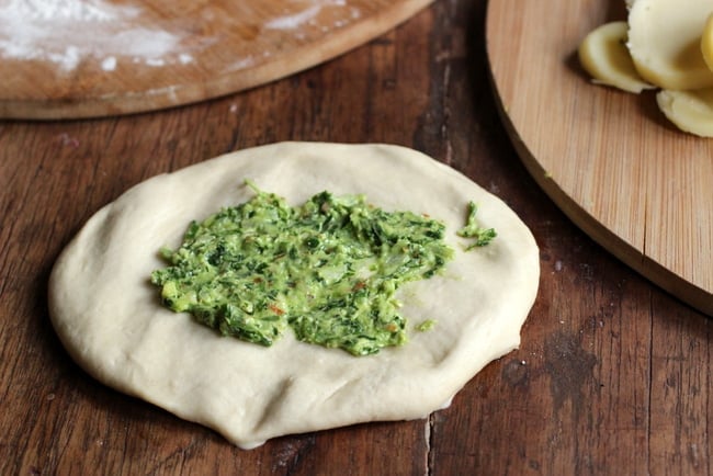 Raw disc of naan dough with pesto in the middle on wooden table.
