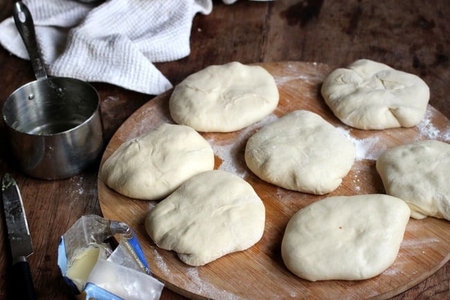 Wooden board with raw naan rounds, steel cup, white cloth.