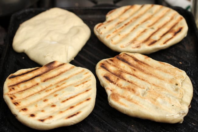 Grilling four naan rounds on a cast iron skillet.