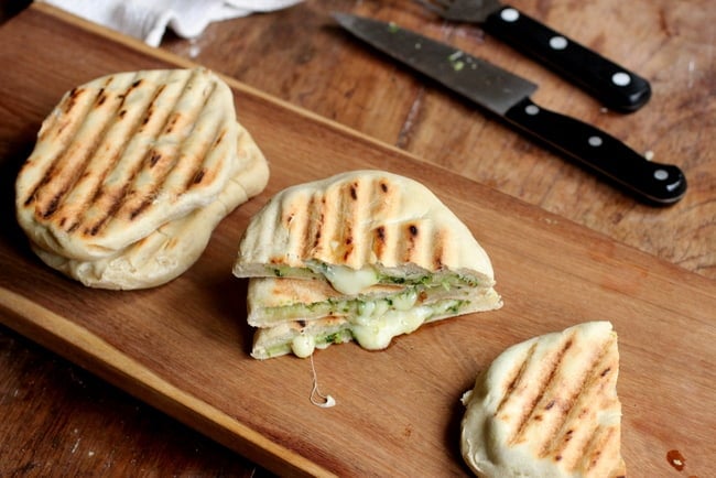 Several cheese filled naan, whole and halved, on a wooden board. 