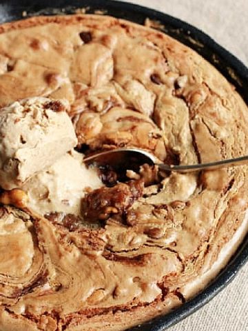 Close up of cast iron skillet with peanut butter blondies, ice cream scoop and spoon.