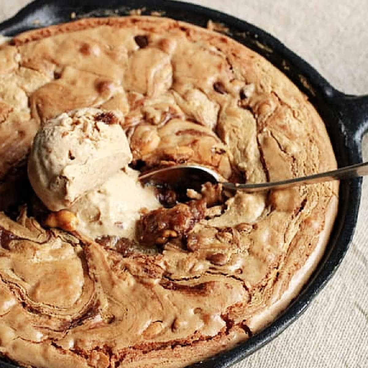 Close up of cast iron skillet with peanut butter blondies, ice cream scoop and spoon.