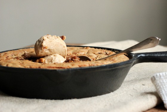 Front view of cast iron skillet with scoop of ice cream over baked blondies. Beige surface and grey background. 