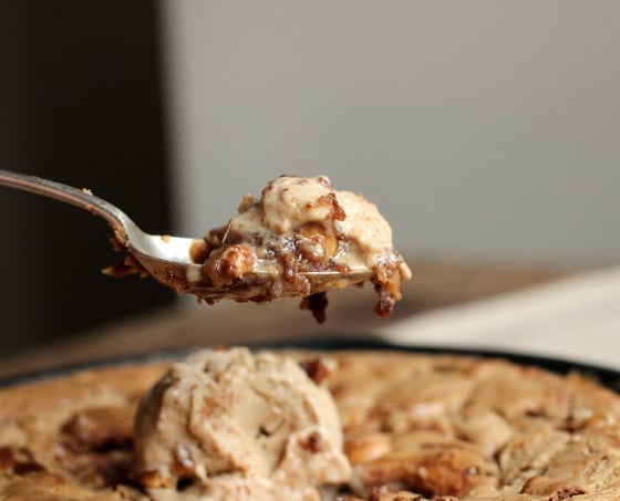 Silver spoon with bite of blondies and ice cream. Skillet with rest of dessert below. Grey beige background. 