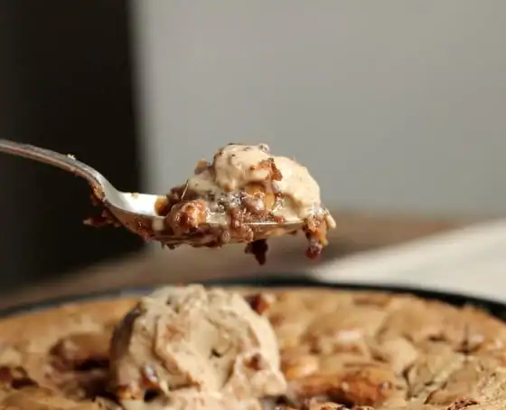 Silver spoon with bite of blondies and ice cream. Skillet with rest of dessert below.
