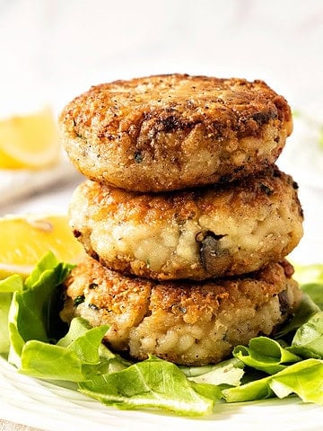 Close up stack of risotto cakes on lettuce leaf. White plate, lemon wedges, white background.